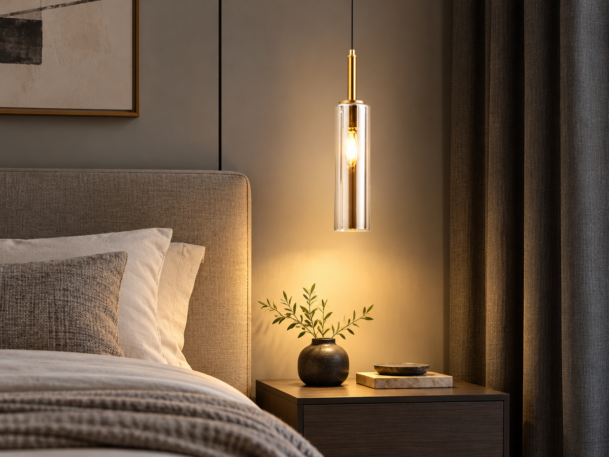 Slim gold and clear cylinder LED pendant beside a bed in a softly lit modern bedroom