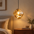 Amber faceted glass pendant glowing beside a bed in a calm neutral bedroom