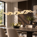 Gold sculptural wave LED pendant installed above a modern dining table