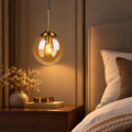 Amber glass globe pendant installed above a refined bedside table