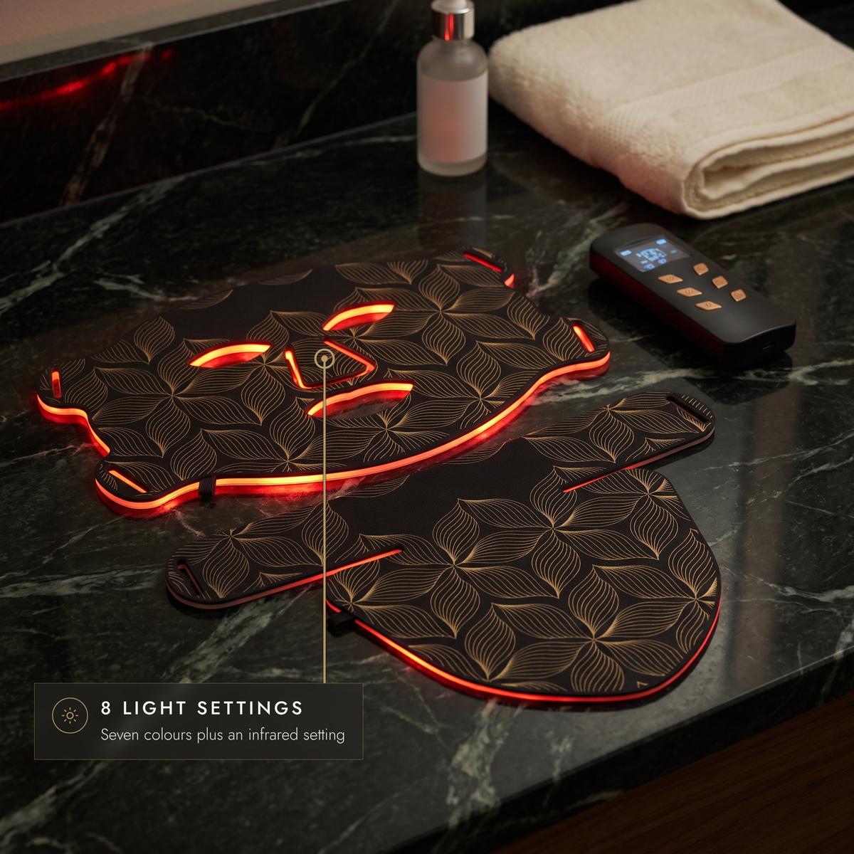 Black and gold LED face mask and neck mask glowing red on a marble vanity with controller