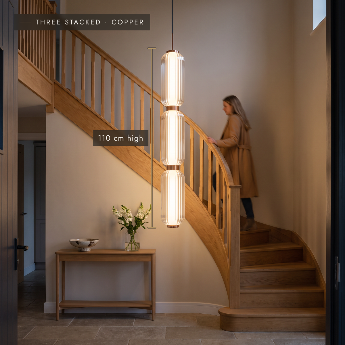 Three stacked ribbed LED pendant in copper finish beside a staircase in an entrance hall