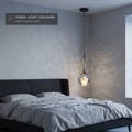 Teardrop pendant light with round flat canopy above a bed in three light colours
